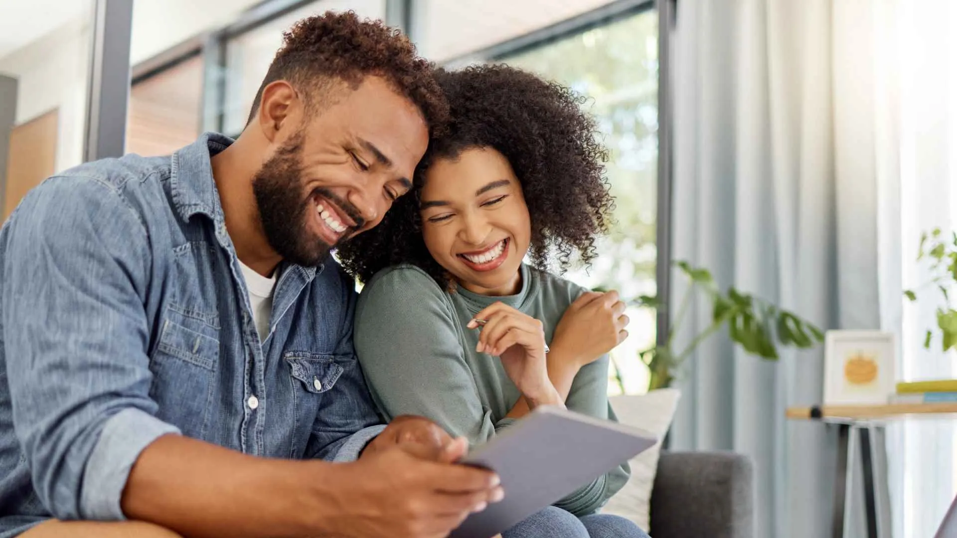 Young happy couple going through documents and using a digital tablet at a table together at home.