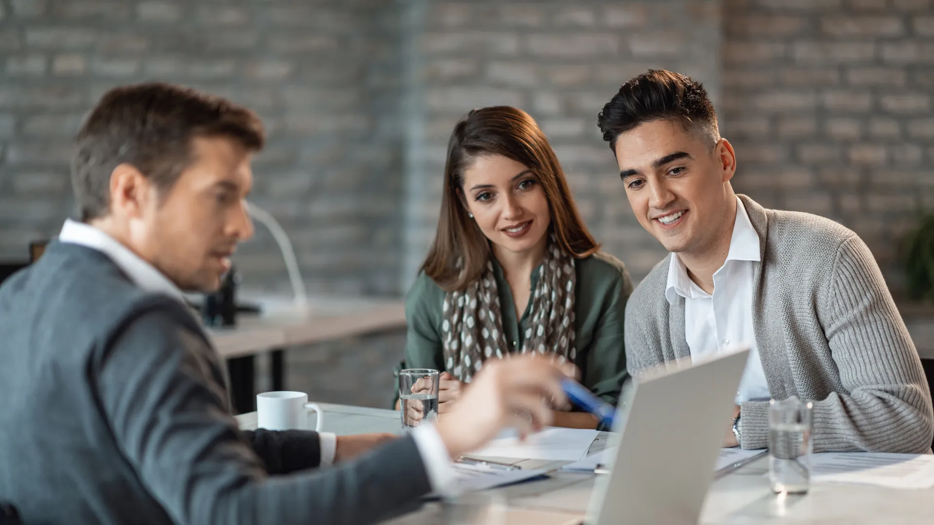 A happy, smiling couple and their financial advisor use a computer during a meeting in the office.