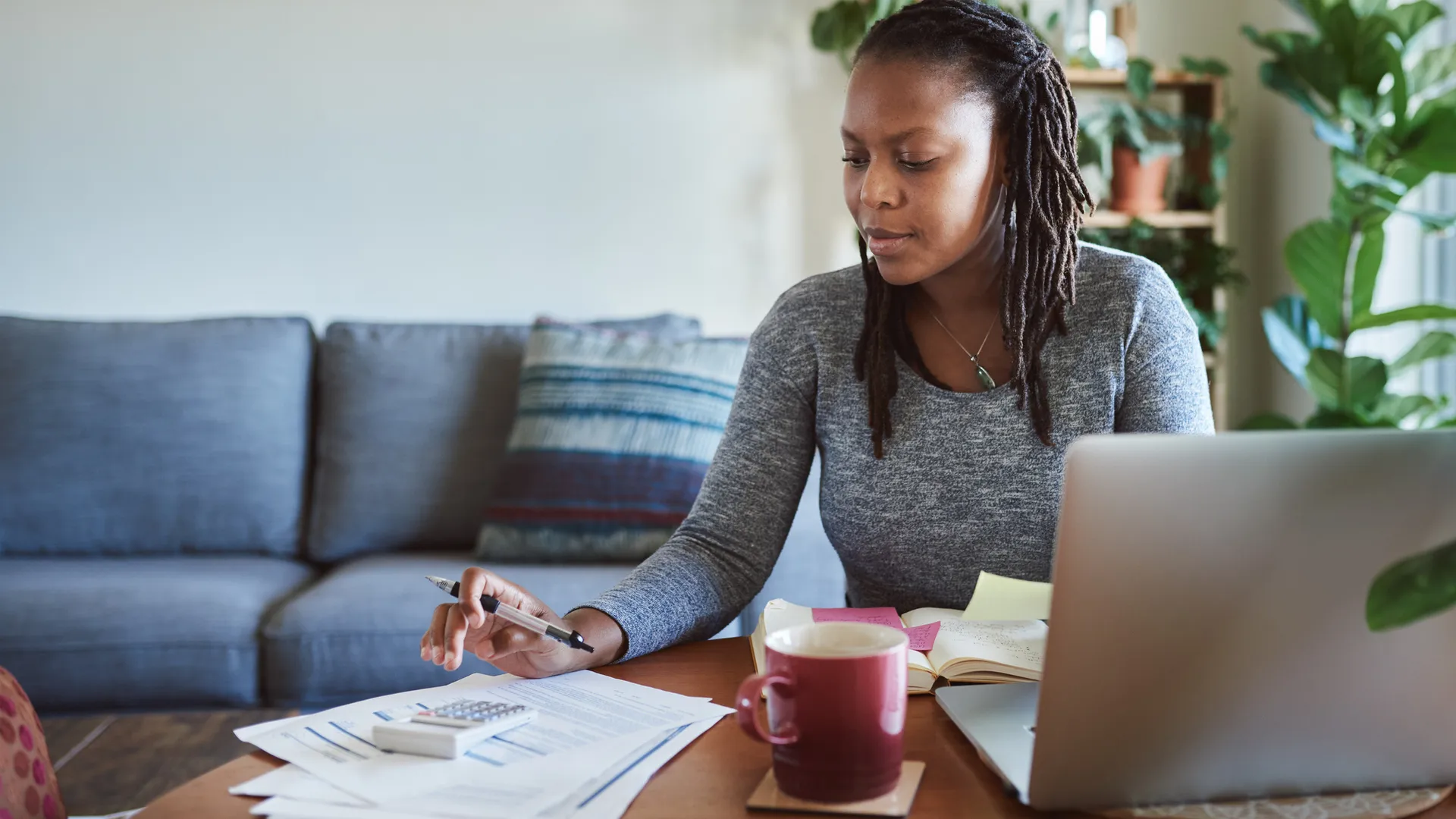 Shot of a young woman using a laptop and going through documents while working from home.