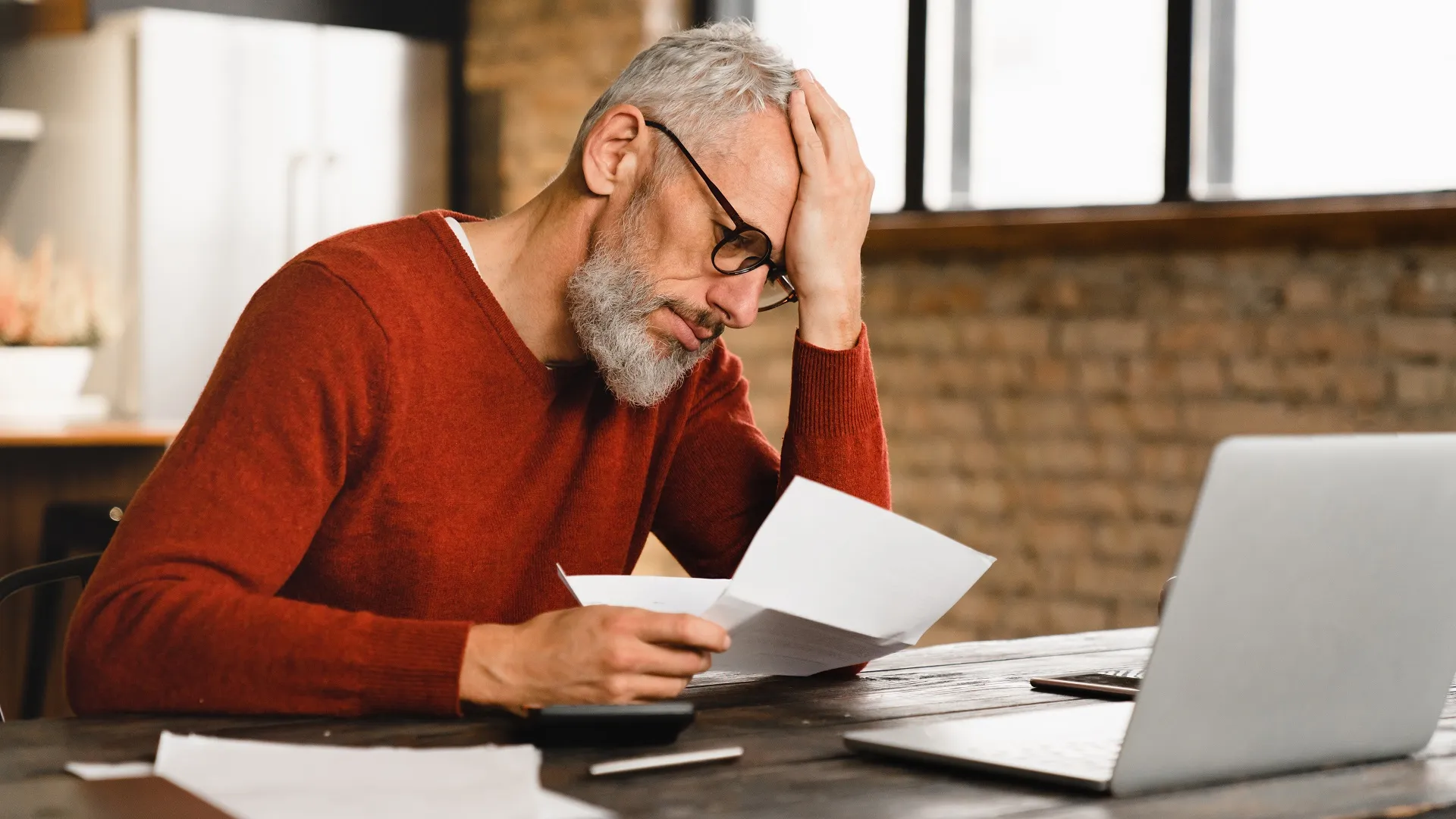 A man holds his head while reading a bill.