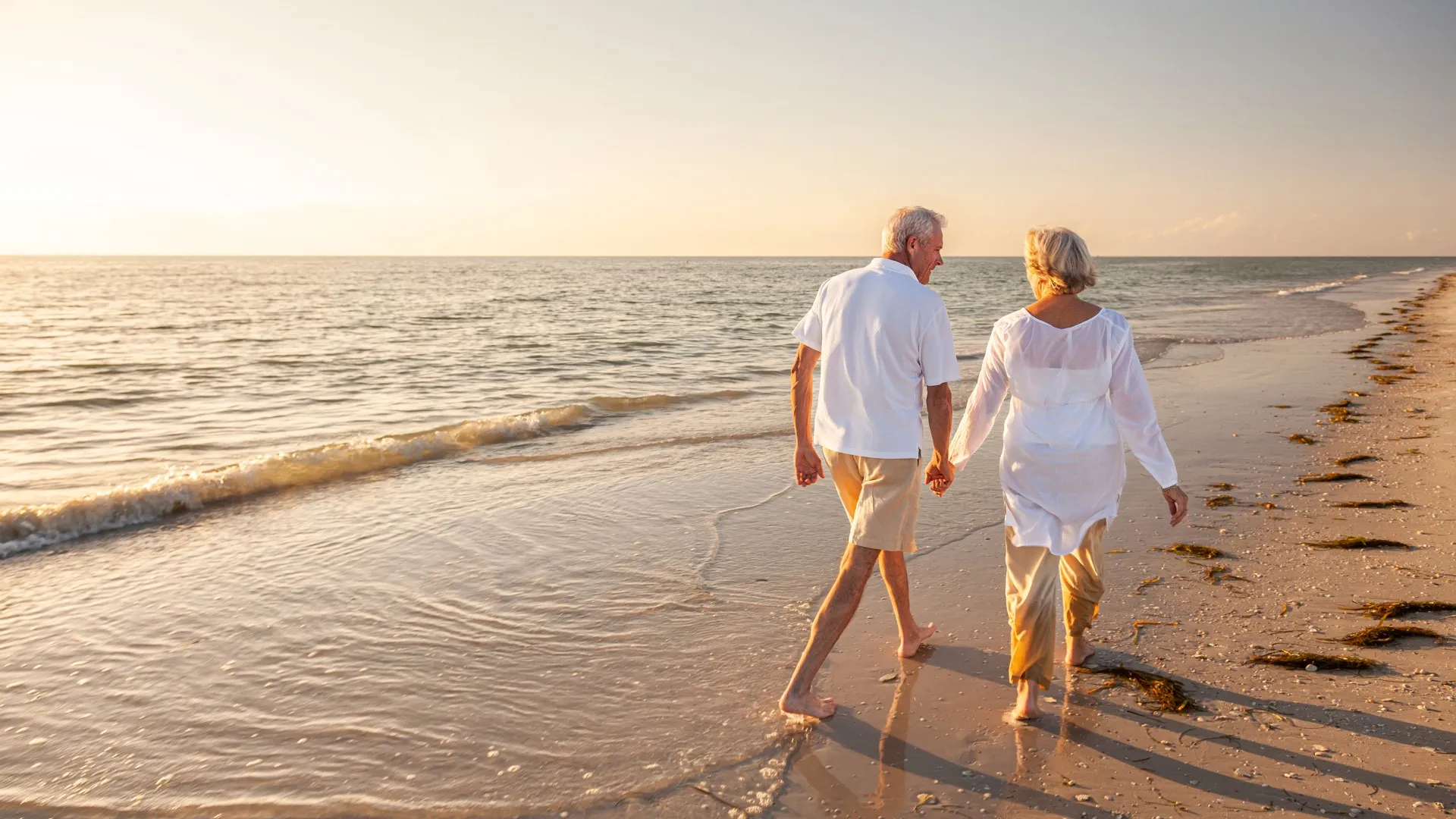 A retired couple walks on the beach.