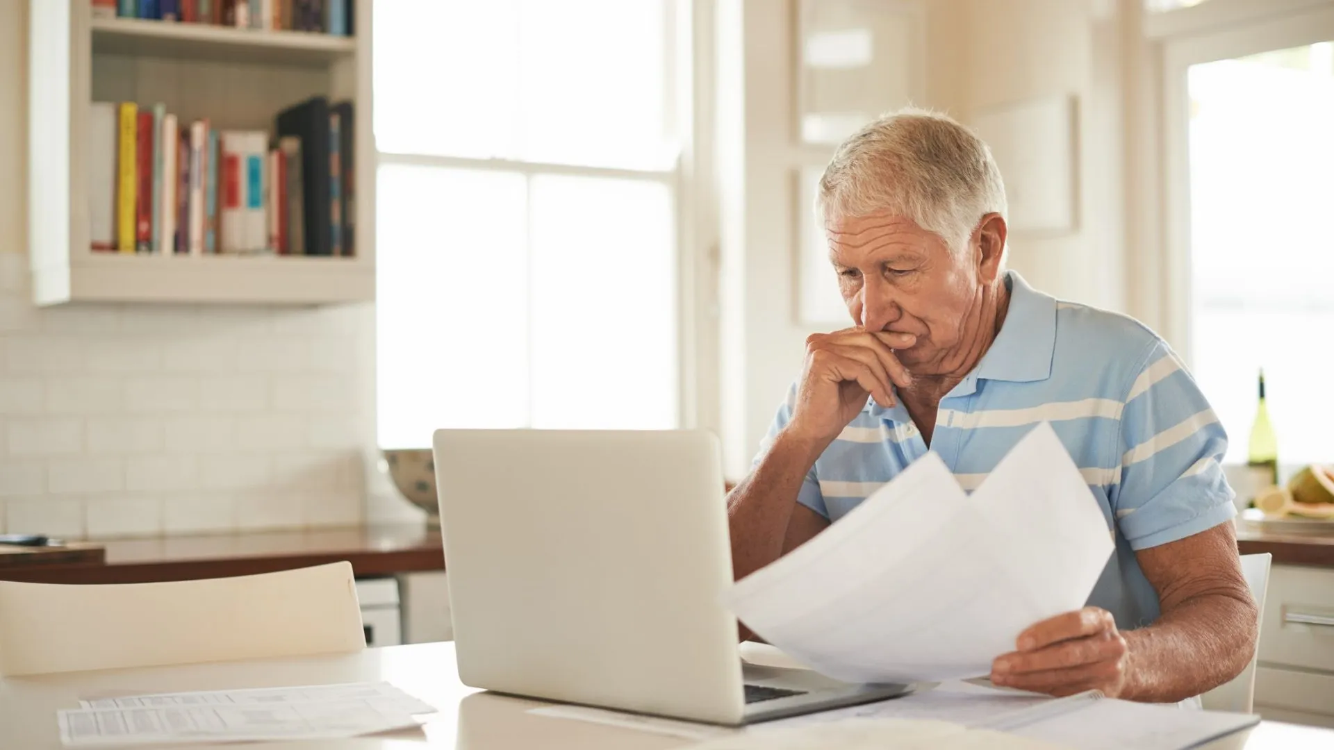 Shot of a senior man looking stressed while doing the household finances on a laptop in his kitchen.