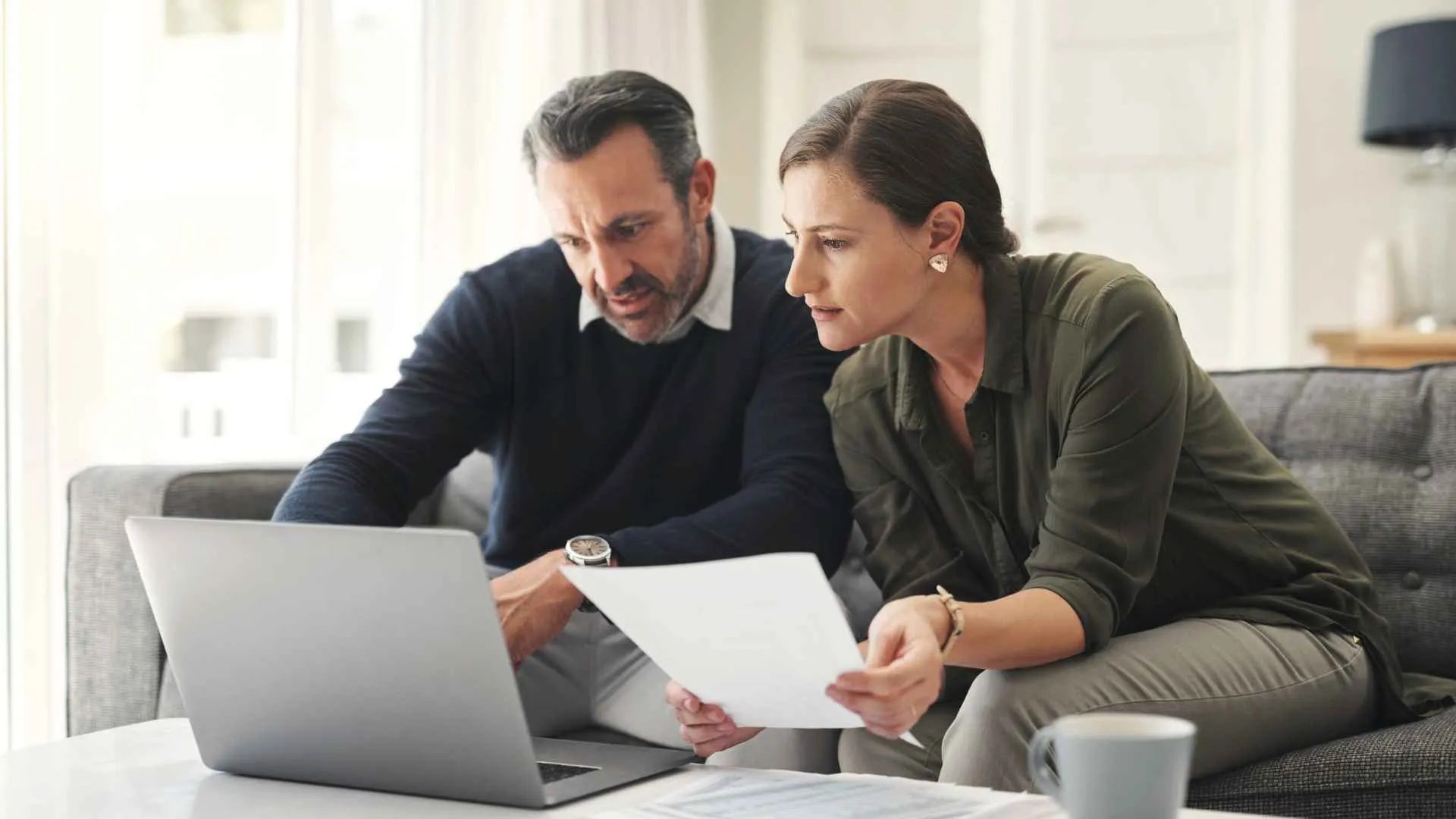 A couple looks at paperwork while sitting in front of a laptop.