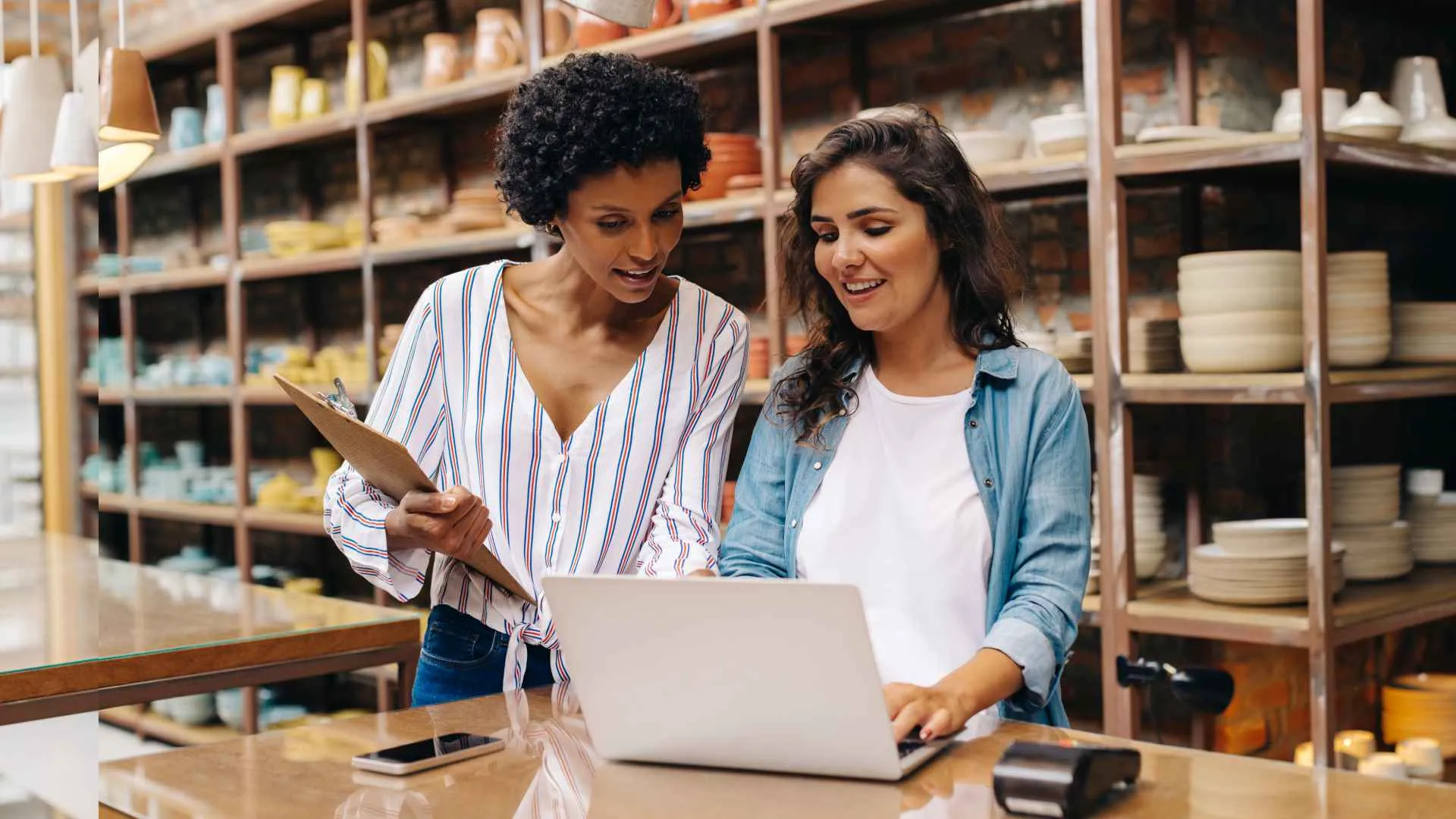 Two young shop owners using a laptop while working in a ceramic store.