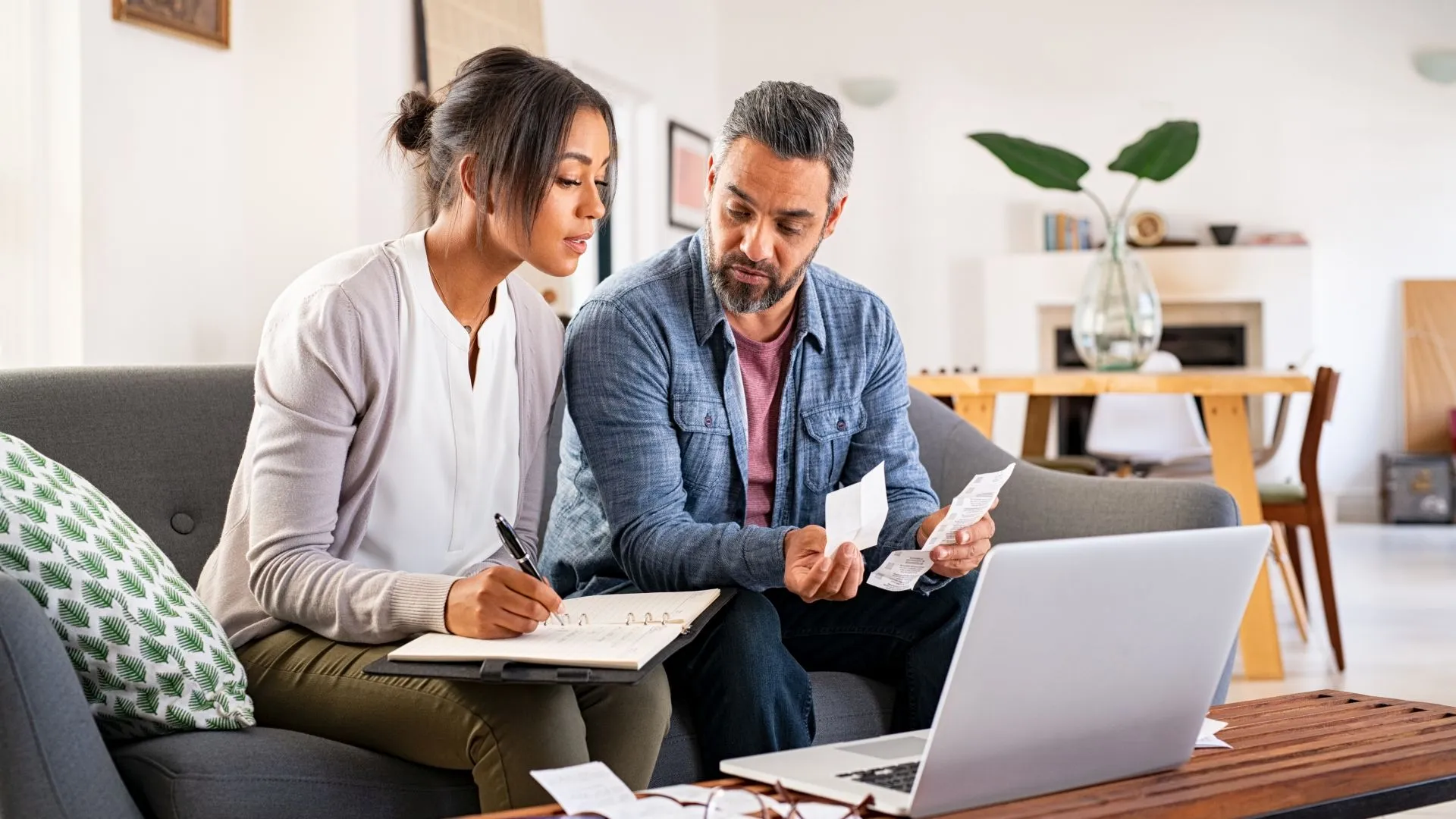 Mature couple calculating bills at home using laptop and calculator.