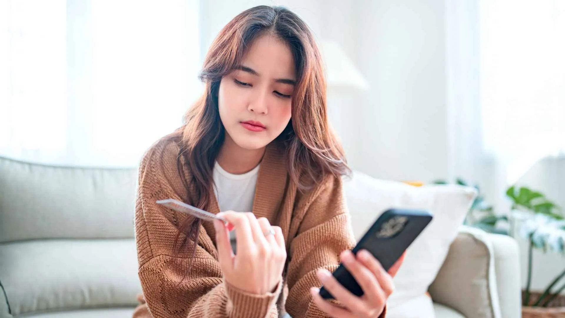 A woman holds a credit card and her phone.