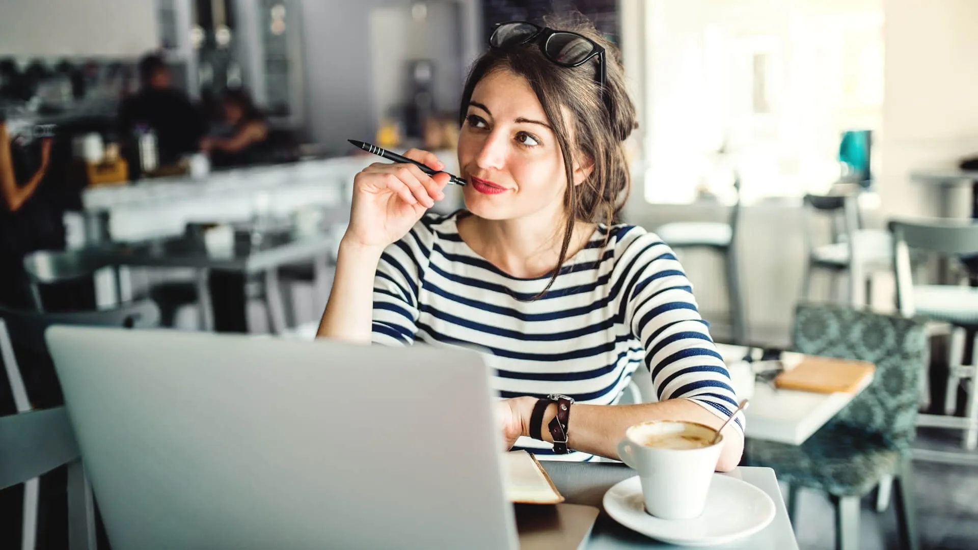 woman with laptop and a cup of coffee sitting in a cafe, writing.